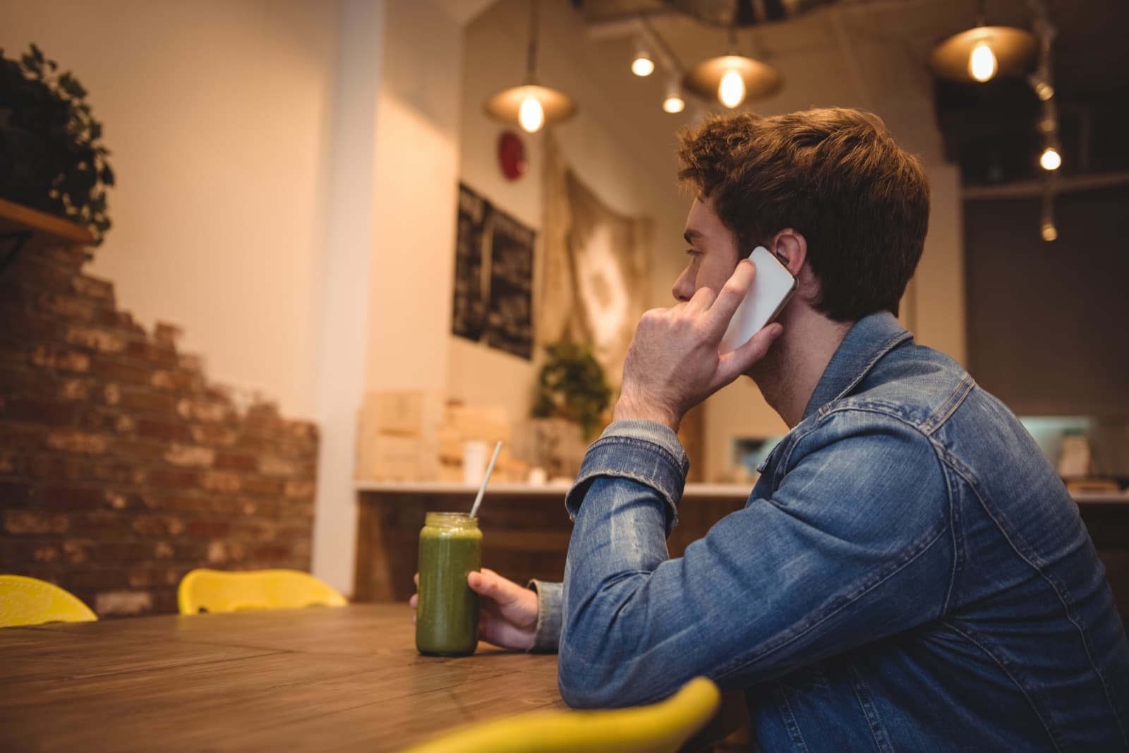 A man on the phone in a café, holding a green smoothie instead of a drink